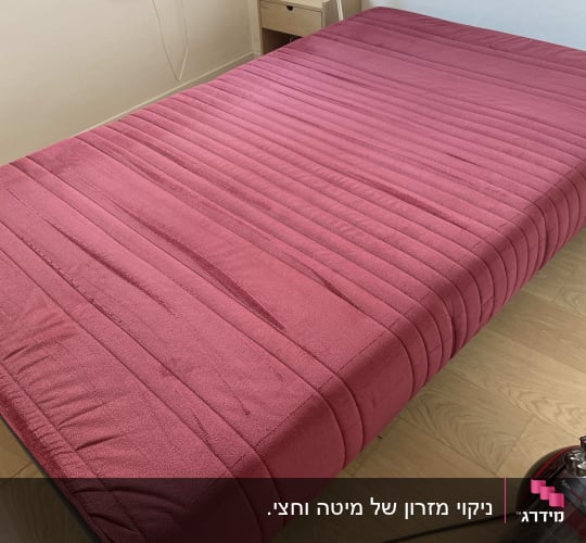מיטה עם כיסוי ורוד ושואב אבק בצד